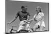 1930s 1940s SMILING BLONDE COUPLE ON BIKES LOOKING AT ONE ANOTHER-H. Armstrong Roberts-Mounted Photographic Print