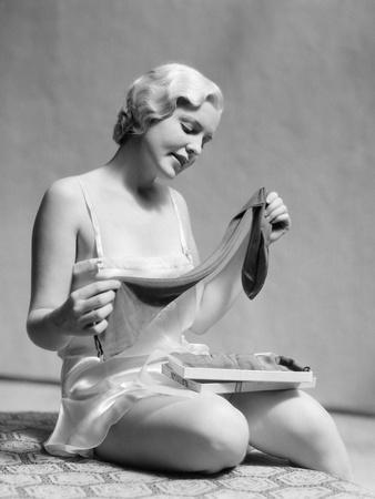 1930s BLOND WOMAN IN SILK TEDDY LINGERIE OPENING A BOX OF HOSIERY