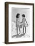 1930s TWO SMILING GIRLS SISTERS FRIENDS HOLDING HANDS AND SAND PAIL AND SHOVEL WALKING ON SAND DUNE-H. Armstrong Roberts-Framed Photographic Print