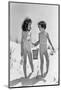 1930s TWO SMILING GIRLS SISTERS FRIENDS HOLDING HANDS AND SAND PAIL AND SHOVEL WALKING ON SAND DUNE-H. Armstrong Roberts-Mounted Photographic Print