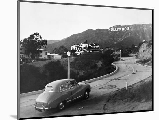 1950s AUSTIN CAR DRIVING UP THE HOLLYWOOD HILLS WITH HOLLYWOOD SIGN IN DISTANCE LOS ANGELES CA USA-Panoramic Images-Mounted Photographic Print