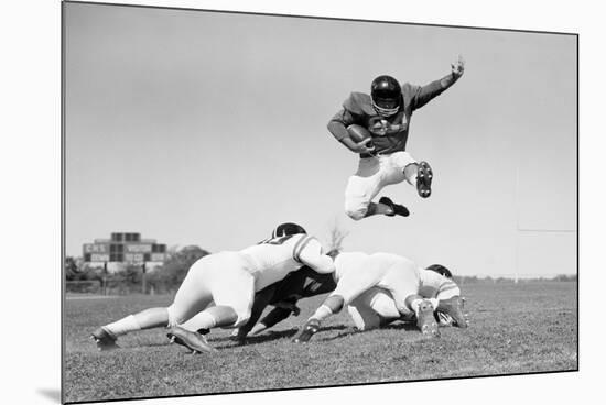 1960s FOOTBALL PLAYER JUMPING OVER BLOCKED PLAYERS-H. Armstrong Roberts-Mounted Photographic Print