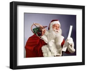 1960s SANTA CLAUS READING THE LIST OF NAUGHTY & NICE SMILING CARRY BAG OF TOYS-Panoramic Images-Framed Photographic Print