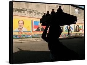 A Boy Carrying Bottles on His Head Passes by a Wall with Pictures of Haitian President Renel Preval-Ariana Cubillos-Framed Stretched Canvas