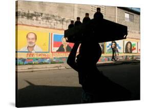 A Boy Carrying Bottles on His Head Passes by a Wall with Pictures of Haitian President Renel Preval-Ariana Cubillos-Stretched Canvas
