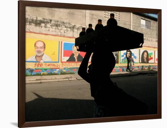 A Boy Carrying Bottles on His Head Passes by a Wall with Pictures of Haitian President Renel Preval-Ariana Cubillos-Framed Photographic Print