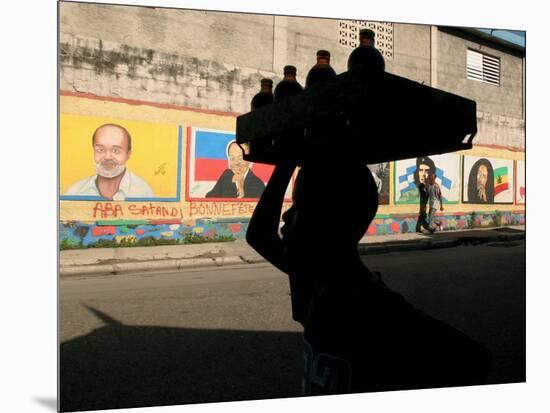 A Boy Carrying Bottles on His Head Passes by a Wall with Pictures of Haitian President Renel Preval-Ariana Cubillos-Mounted Photographic Print