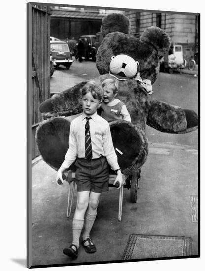 A Boy Gives a Ride to a Little Girl and a 9-Foot Teddy Bear at the Opening of the British Toy Fair-null-Mounted Photographic Print