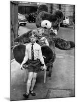 A Boy Gives a Ride to a Little Girl and a 9-Foot Teddy Bear at the Opening of the British Toy Fair-null-Mounted Photographic Print