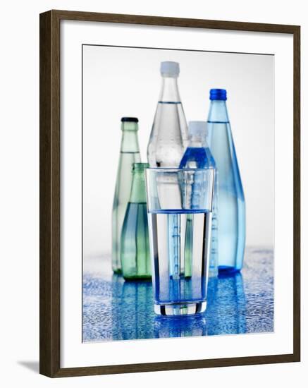 A Glass in Front of Mineral Water Bottles-Alexander Feig-Framed Photographic Print