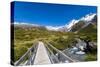 A hiking trail crosses wooden bridge over a creak high up in the mountains, New Zealand-Logan Brown-Stretched Canvas