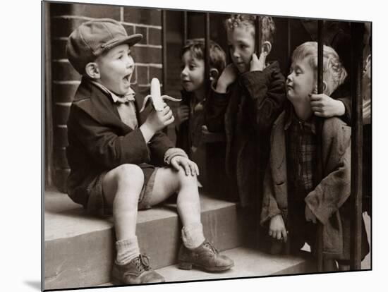 A Little Boy Holding a Banana Whilst Other Children Gaze Longingly at It-null-Mounted Photographic Print
