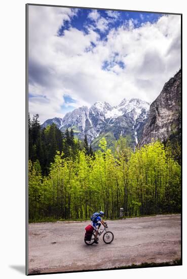 A Lone Cyclist Travels Along a Mountain Road with Trees and the Julian Alps in the Background-Sean Cooper-Mounted Photographic Print