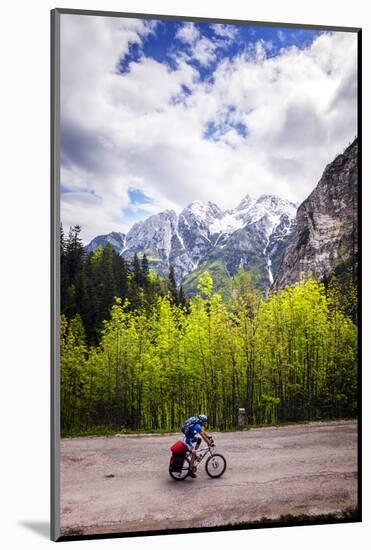 A Lone Cyclist Travels Along a Mountain Road with Trees and the Julian Alps in the Background-Sean Cooper-Mounted Photographic Print