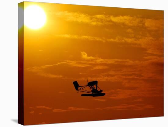 A Pilot Flies a Small Plane Past the Setting Sun Over Lake Winnipesaukee-null-Stretched Canvas