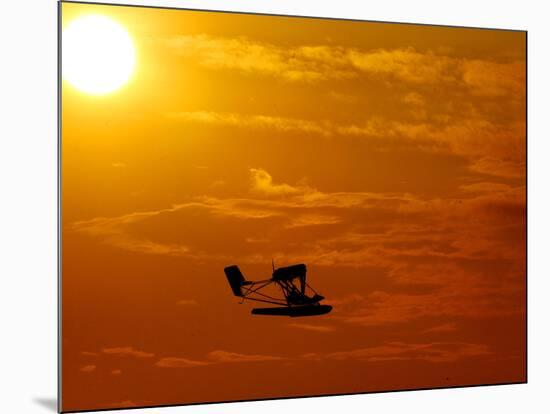 A Pilot Flies a Small Plane Past the Setting Sun Over Lake Winnipesaukee-null-Mounted Photographic Print