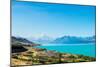 A road winds along the edge of a turquoise blue lake with mountains in the distance, New Zealand-Logan Brown-Mounted Photographic Print