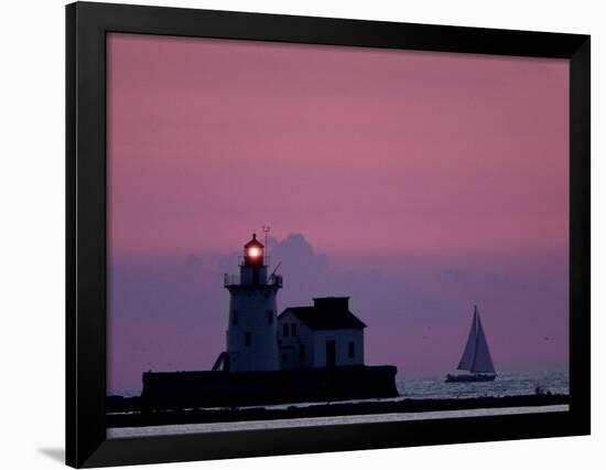 A Sailboat Slips Past a Lighthouse as the Sunset Comes to Lake Erie off the Coast of Cleveland-null-Framed Photographic Print