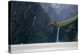 A sightseeing ship dwarfed by a tall waterfall in a fjord, South Island, New Zealand, Pacific-Logan Brown-Stretched Canvas