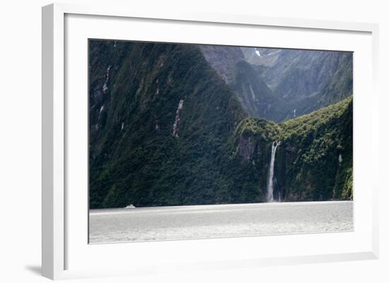 A sightseeing ship dwarfed by a tall waterfall in a fjord, South Island, New Zealand, Pacific-Logan Brown-Framed Photographic Print