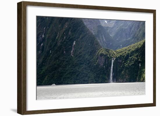 A sightseeing ship dwarfed by a tall waterfall in a fjord, South Island, New Zealand, Pacific-Logan Brown-Framed Photographic Print