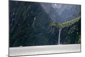 A sightseeing ship dwarfed by a tall waterfall in a fjord, South Island, New Zealand, Pacific-Logan Brown-Mounted Photographic Print