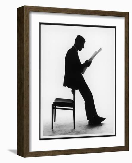 A Silhouette of a Businessman Leaning Against a Chair Reading a Newspaper-null-Framed Photographic Print