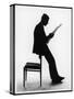 A Silhouette of a Businessman Leaning Against a Chair Reading a Newspaper-null-Stretched Canvas
