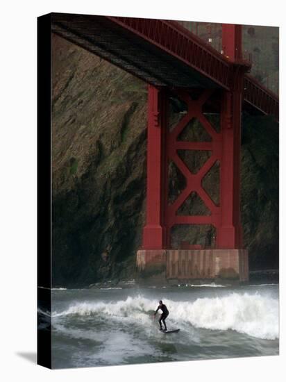 A Surfer is Dwarfed by the Northern End of the Golden Gate Bridge While Riding the Waves-null-Stretched Canvas