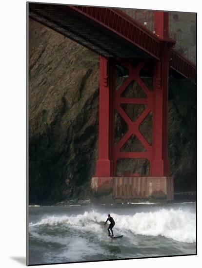 A Surfer is Dwarfed by the Northern End of the Golden Gate Bridge While Riding the Waves-null-Mounted Premium Photographic Print