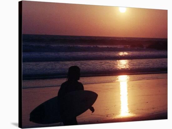 A Surfer is Silhouetted by the Setting Sun as He Leaves the Pacific Ocean on Venice Beach-null-Stretched Canvas