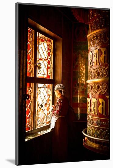 A Tibetan woman stands next to a large prayer wheel of the temple of Boudhanath Stupa, Kathmandu, N-Julian Bound-Mounted Photographic Print