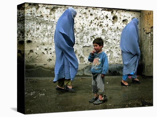 A Young Afghan Refugee Boy Stands in a Pair of Adult's Shoes-null-Stretched Canvas