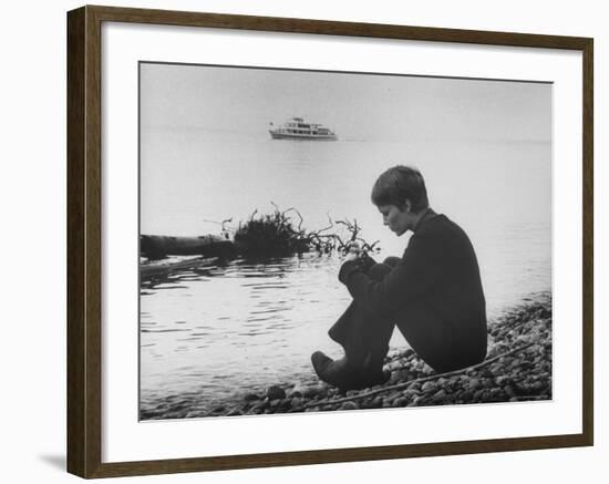 Actress Mia Farrow Pensively Sitting on Rocky Shore of Lake Geneva as Passenger Boat Passes By-Bill Eppridge-Framed Premium Photographic Print