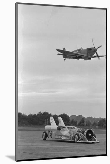 Airplane Flying over Race Car in Action-null-Mounted Photographic Print