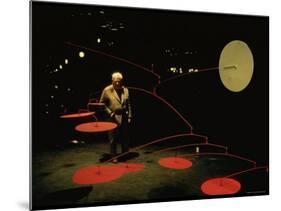 Alexander Calder Walking Past Exhibit of His Mobiles at the Guggenheim Museum-Gjon Mili-Mounted Premium Photographic Print