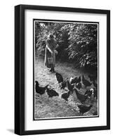 An Older Woman in a Long Dress and Wide-Brimmed Hat Throws Handfuls of Chicken Feed-null-Framed Art Print