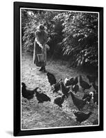 An Older Woman in a Long Dress and Wide-Brimmed Hat Throws Handfuls of Chicken Feed-null-Framed Art Print