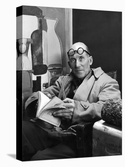 Architect Le Corbusier Sitting in Chair and Holding Book in Hands-Nina Leen-Stretched Canvas