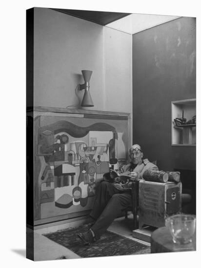 Architect Le Corbusier Sitting in Chair with Book in Hands, Glasses Perched on His Forehead-Nina Leen-Stretched Canvas