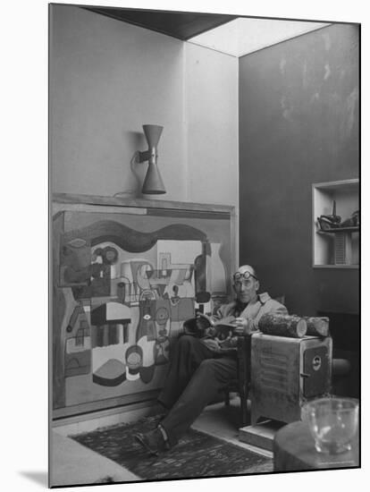 Architect Le Corbusier Sitting in Chair with Book in Hands, Glasses Perched on His Forehead-Nina Leen-Mounted Premium Photographic Print
