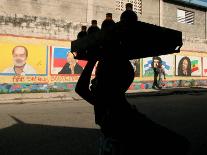 A Boy Carrying Bottles on His Head Passes by a Wall with Pictures of Haitian President Renel Preval-Ariana Cubillos-Framed Stretched Canvas