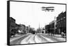 Biplane over a Small Town-J.H. Cave-Framed Stretched Canvas