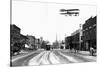 Biplane over a Small Town-J.H. Cave-Stretched Canvas