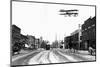 Biplane over a Small Town-J.H. Cave-Mounted Photographic Print