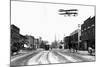 Biplane over a Small Town-J.H. Cave-Mounted Photographic Print