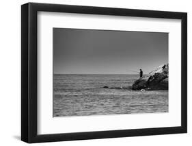 Black and White shot of a lone fisherman on rocks at the beach-null-Framed Photo