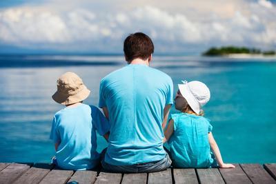 Back View of Father and Kids Sitting on Wooden Dock Looking to Ocean