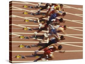 Blurred Action of Male Runners Starting a 100 Meter Sprint Race-Paul Sutton-Stretched Canvas
