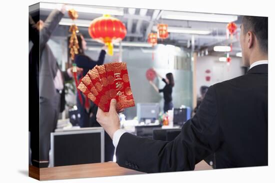 Businessman Holding Red Envelopes and Coworkers Hanging Decorations for Chinese New Year-XiXinXing-Stretched Canvas